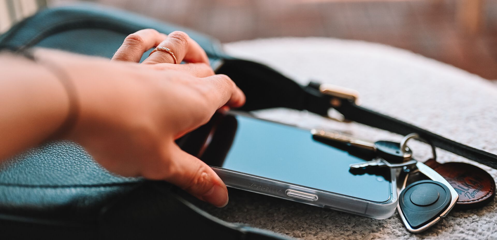 Hand reaching for a smartphone on a table with keys and a wallet.